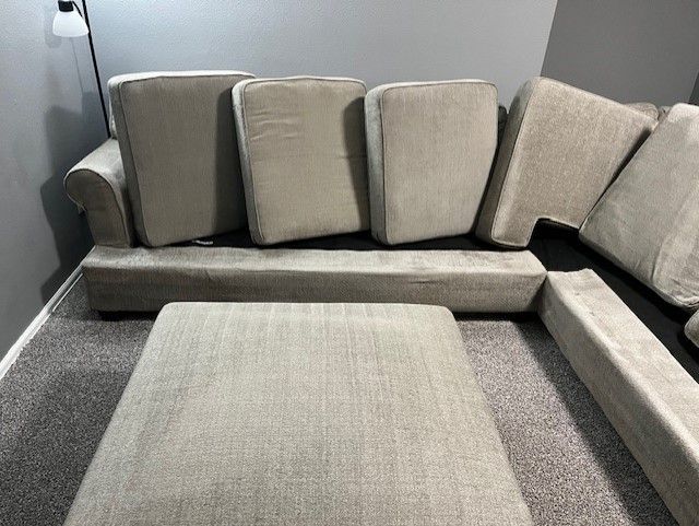 A couch and ottoman are sitting on a carpeted floor in a living room.