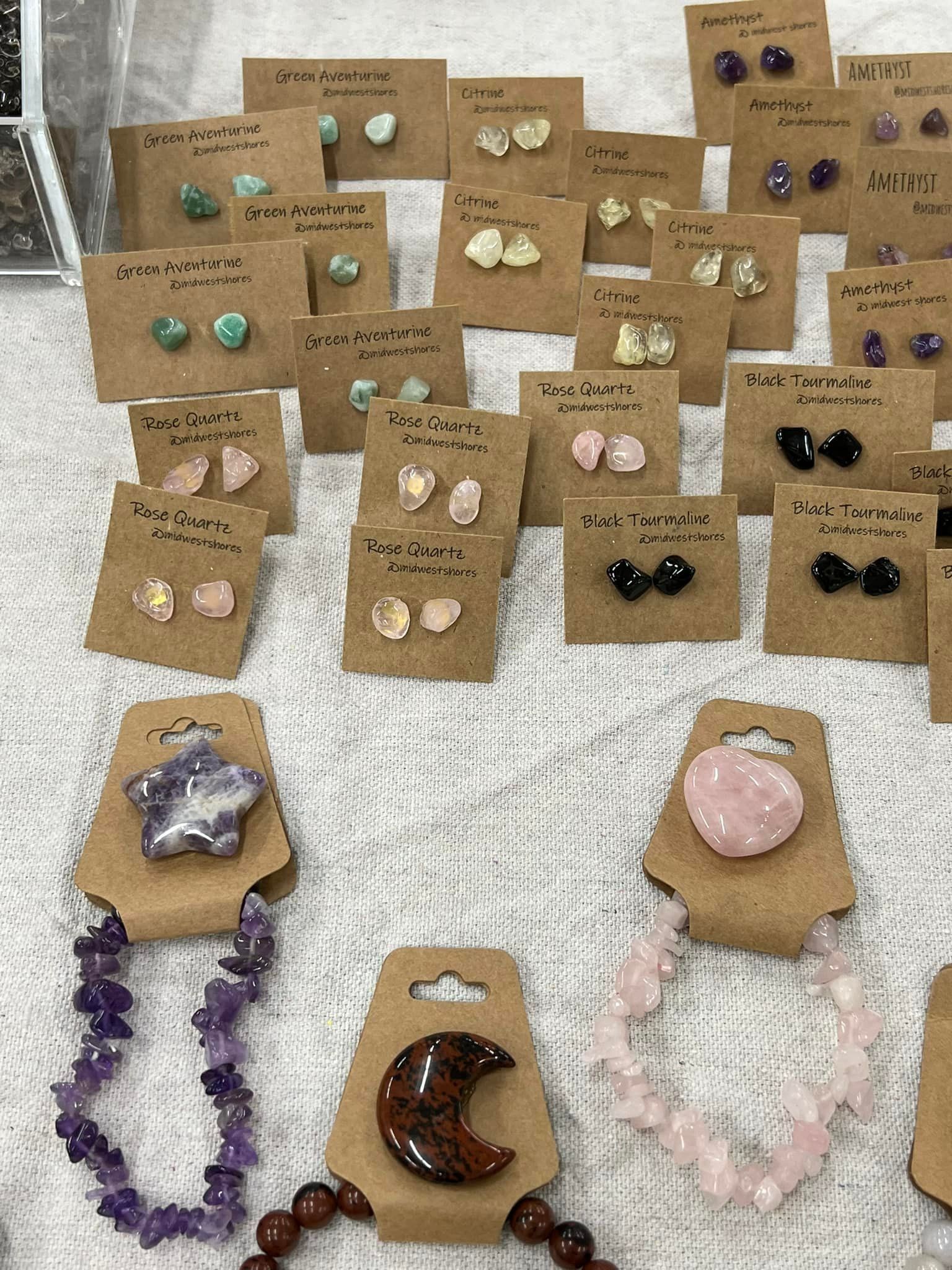 Assorted gemstone earrings and pendant necklaces displayed on brown kraft cards and stone stands.
