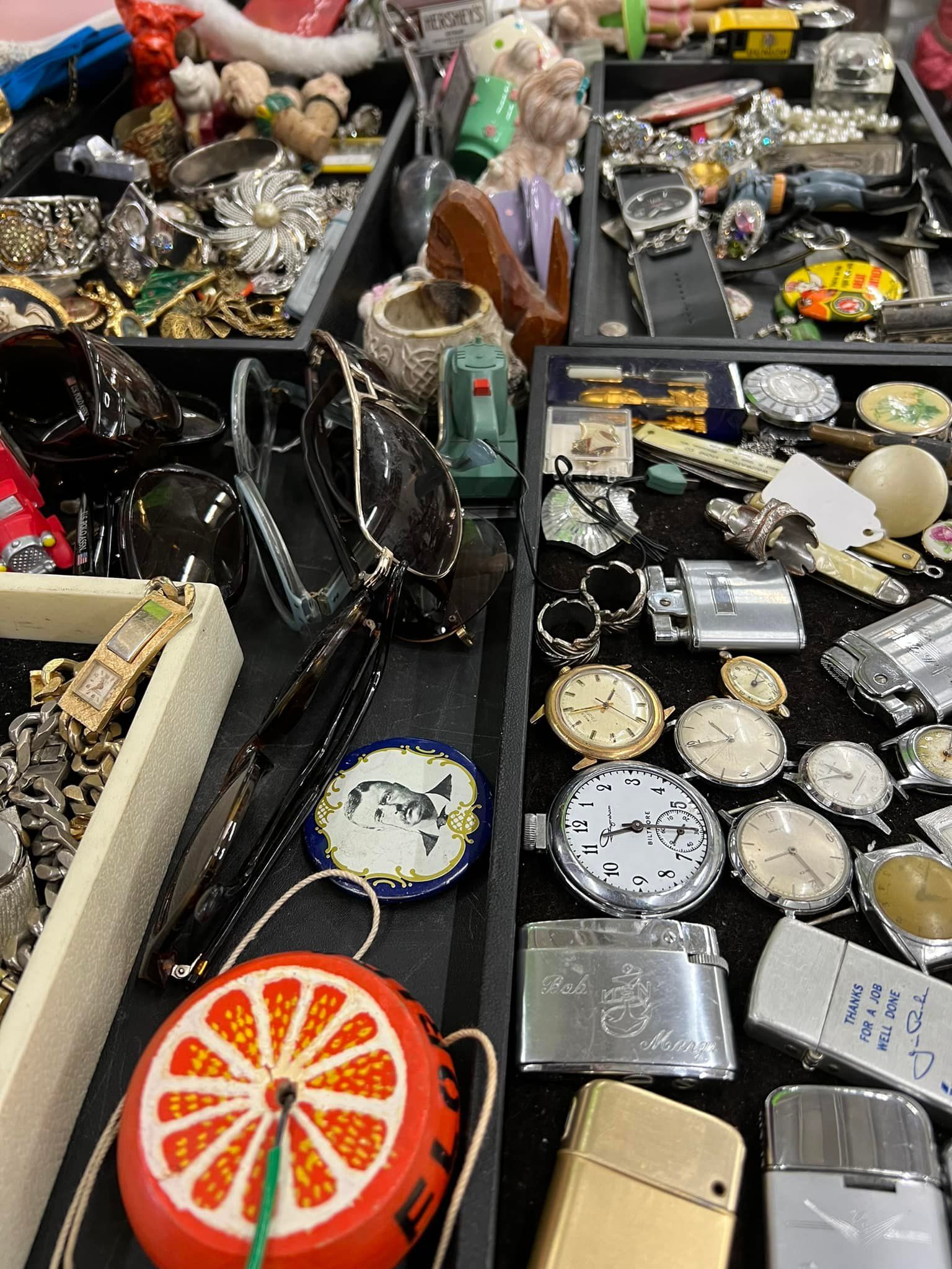 Open display of assorted jewelry, watches, and accessories in trays and cases on a market stall