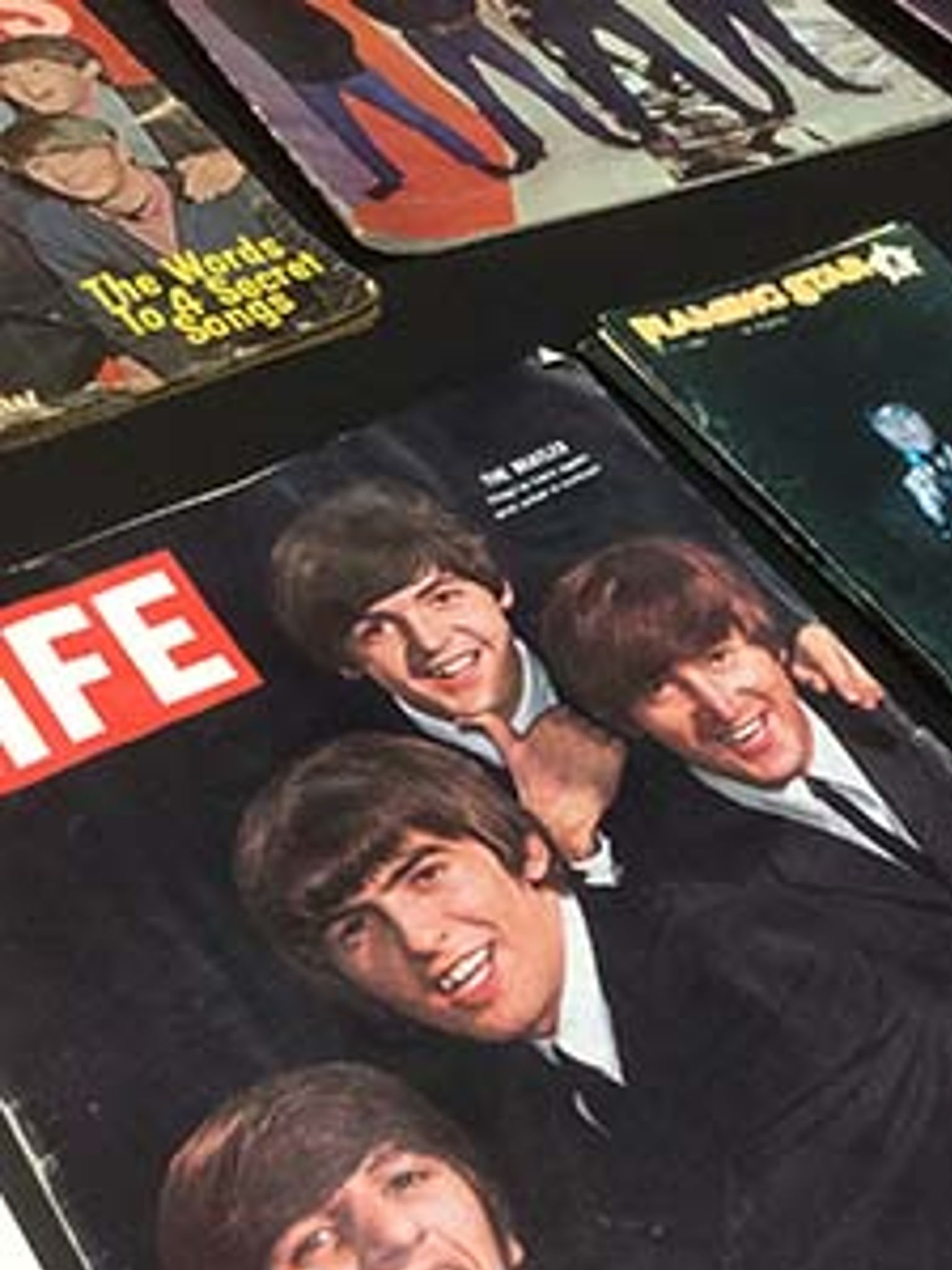 Stack of vintage magazine covers, including LIFE, with a smiling Beatles cover on top.