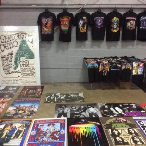 Merch display with colorful graphic T-shirts, posters, and prints on a table and wall in a shop.