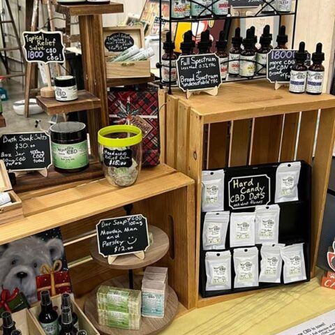 Market display of CBD products in wooden crates, with jars, bottles, and small chalkboard signs.