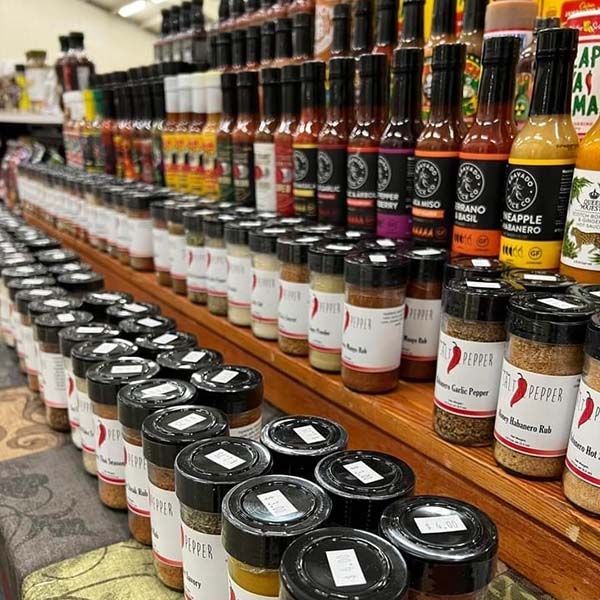 Rows of bottled sauces and spices on store shelves, with black-lidded jars in the foreground.