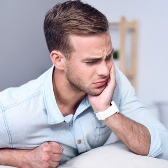Man holding his jaw, showing pain; in a light-colored shirt, indoors.