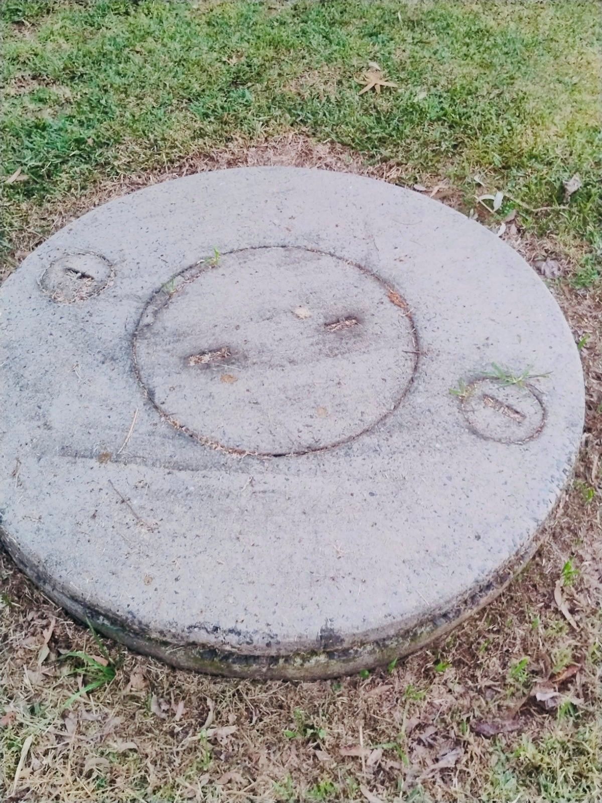 Two concrete septic tanks with green lids in a sandy excavation site, connected by piping.