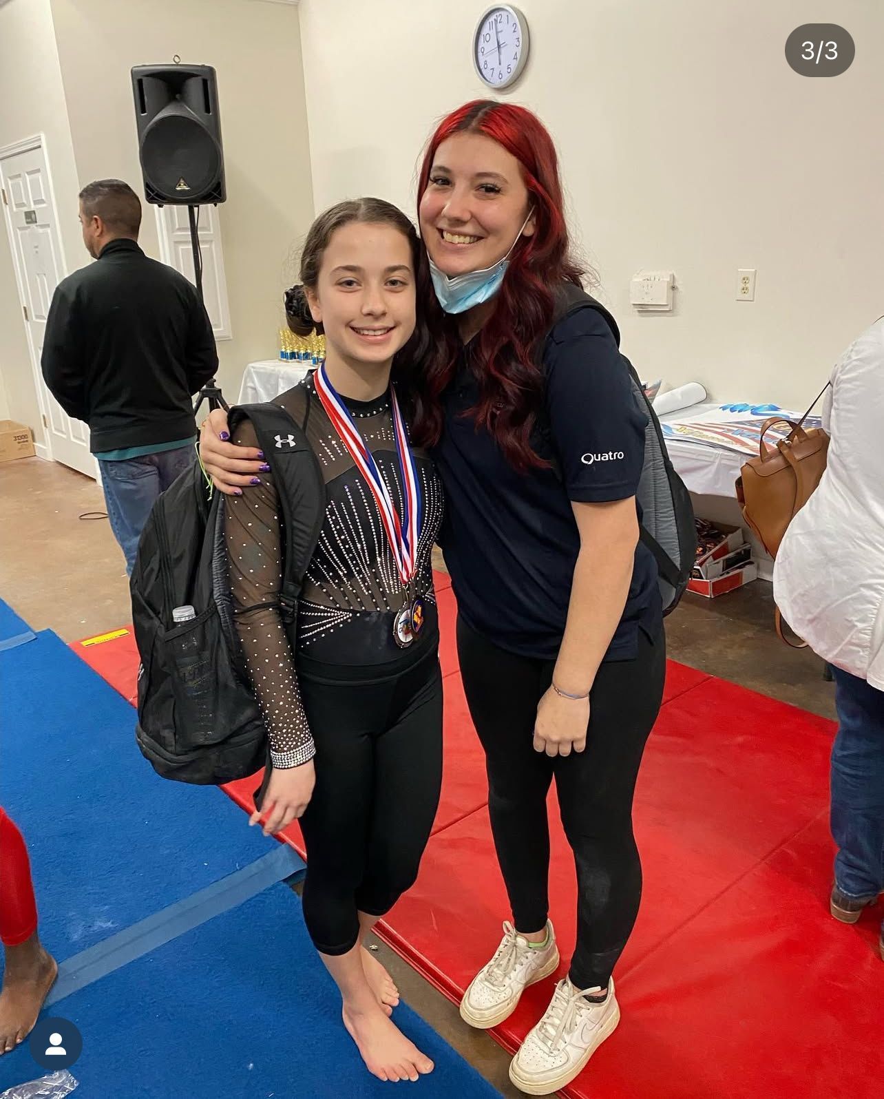 Gymnast with medal and coach smiling, posing together, gymnasium setting.