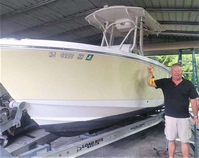 Man standing beside a large white boat on a trailer under a covered shed