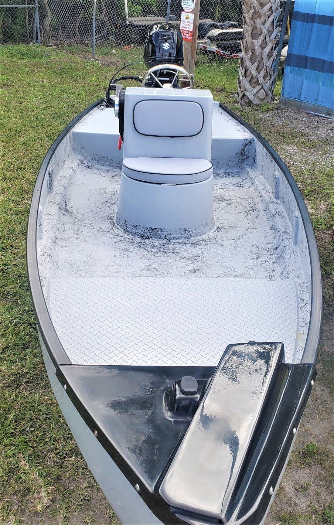 A gray, flat-bottomed skiff boat seen from the bow, featuring a central console, textured flooring, and a black nose.
