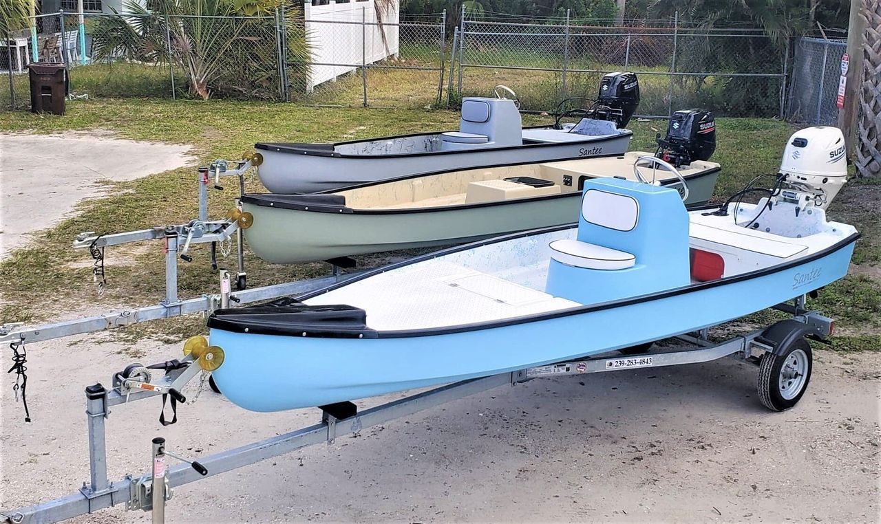 Three small motorboats in shades of blue, green, and gray sit on trailers in a gravel lot.