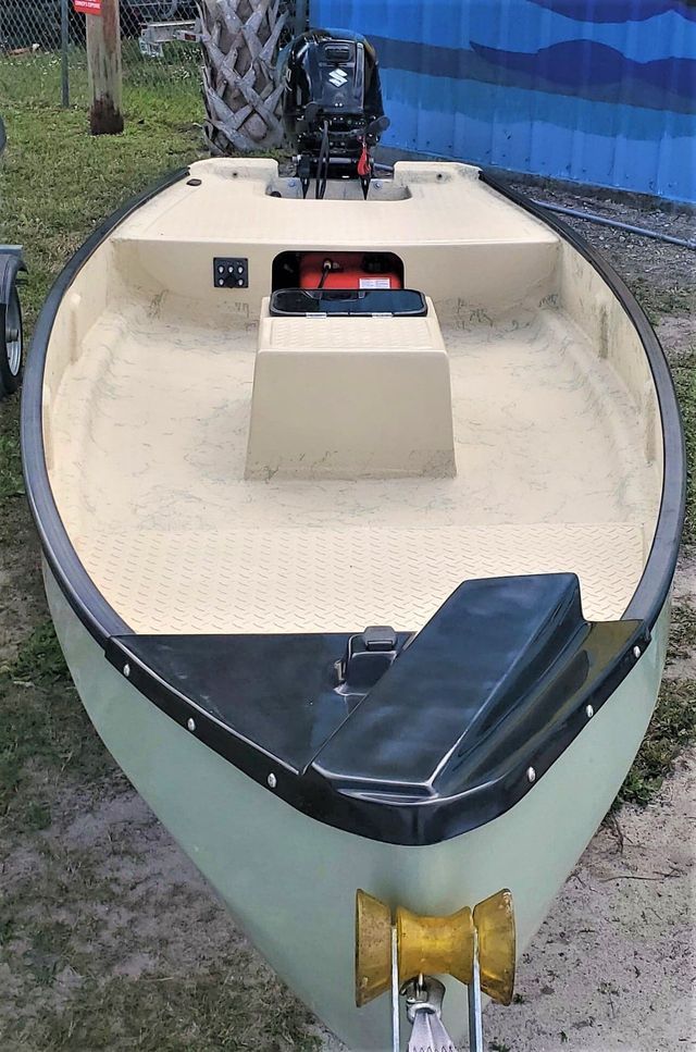 A small, light green skiff boat with a textured tan interior and black trim, docked on land with an outboard motor.