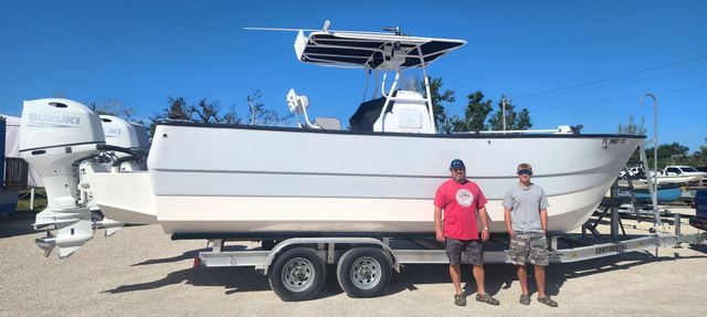 Two people standing beside a white boat on a trailer in a sunny parking lot