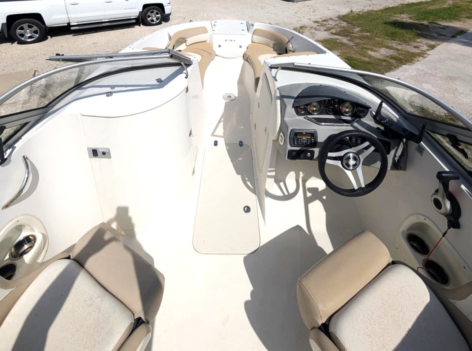 Boat cockpit with cream seats, steering wheel, and windshield on a sunny dock.