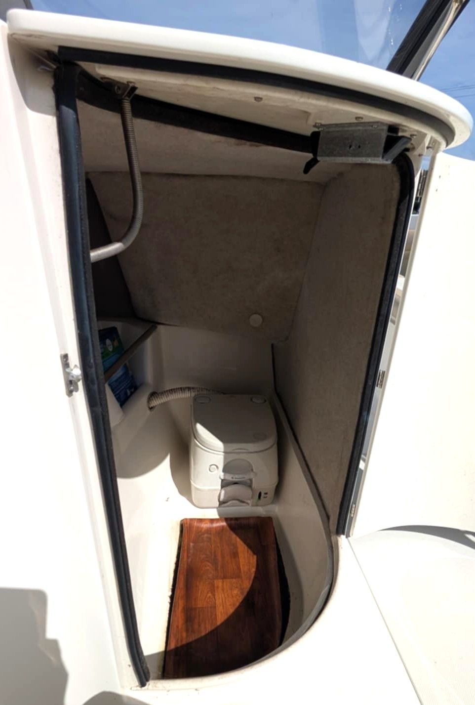 Open white hatch doorway to a small beige storage compartment with a wood floor and stacked white items