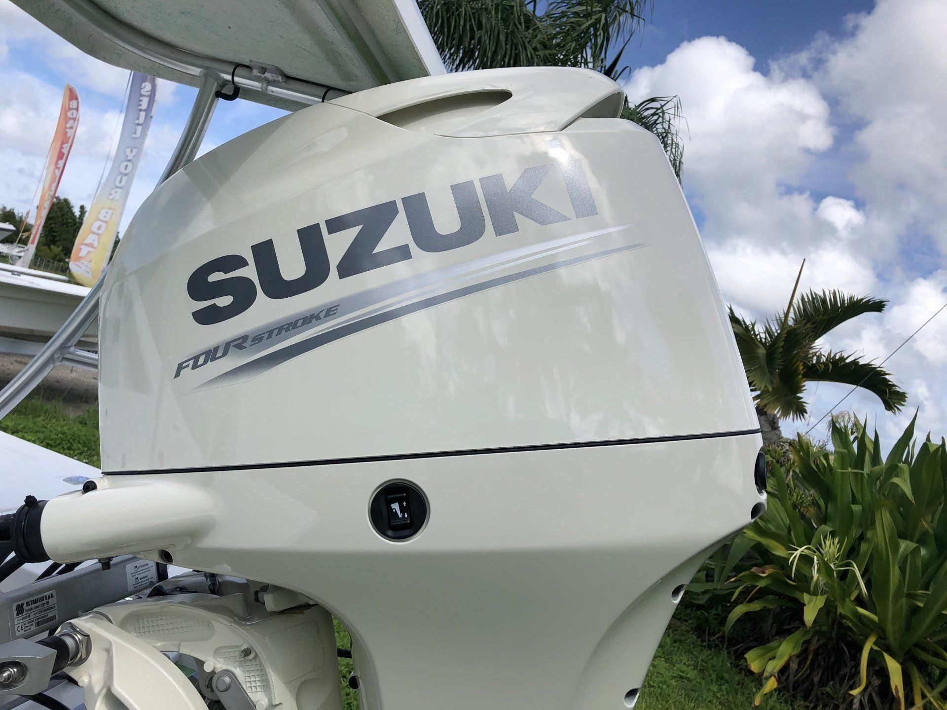 Close-up of a white Suzuki outboard motor on a boat, with palm trees and blue sky in the background
