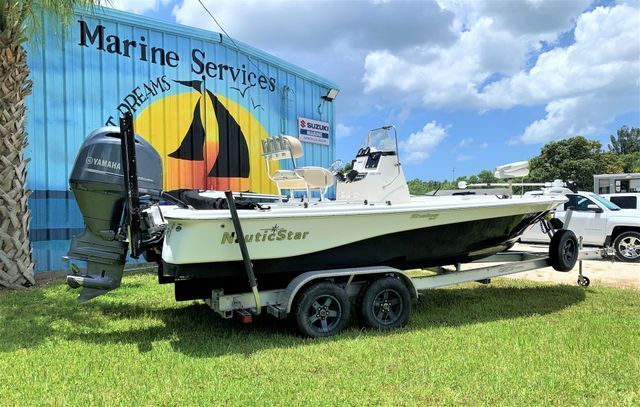 White center-console boat on a trailer in front of a Marine Services sign on a grassy lot.