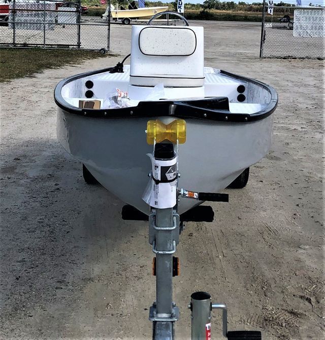 A small, light-grey motorboat on a trailer, viewed from the front, parked on a dirt lot.