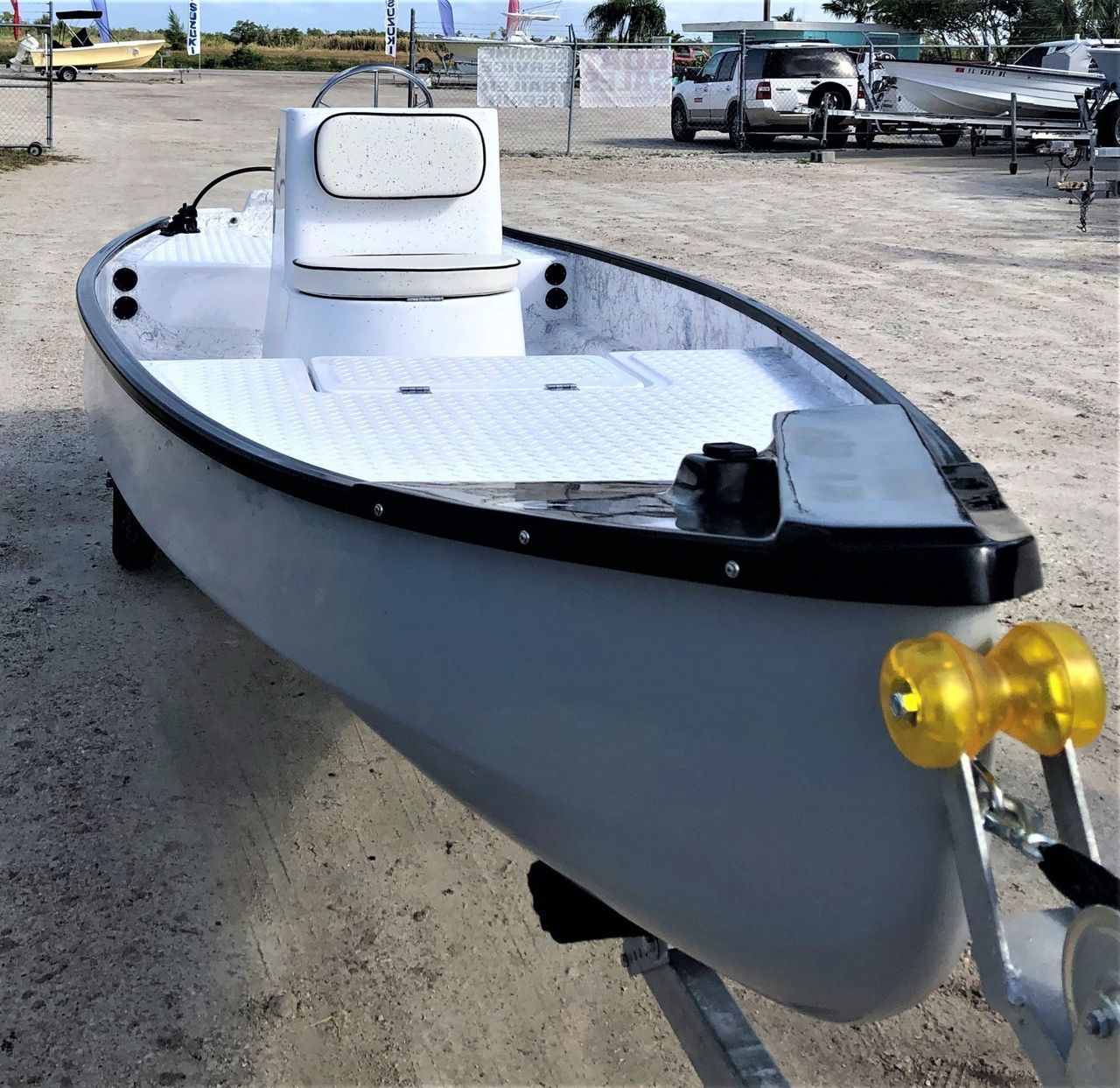 A gray skiff boat with a white center console and interior deck, mounted on a trailer in an outdoor storage lot.