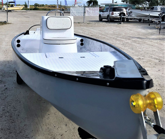 A gray, small center-console boat sits on a trailer in a parking lot, featuring a white deck and a cushioned seat.