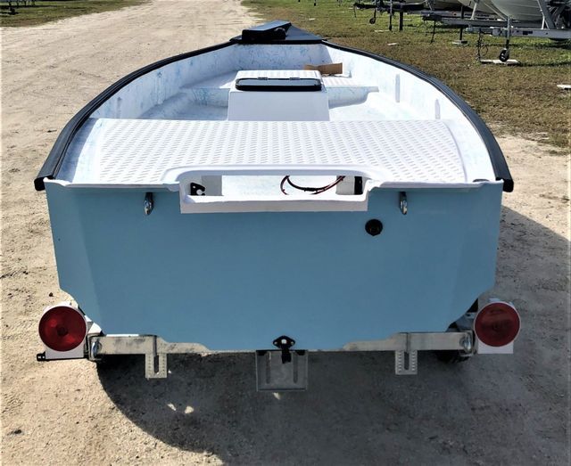 A light blue boat with white interior on a trailer, viewed from the rear on a sandy lot.