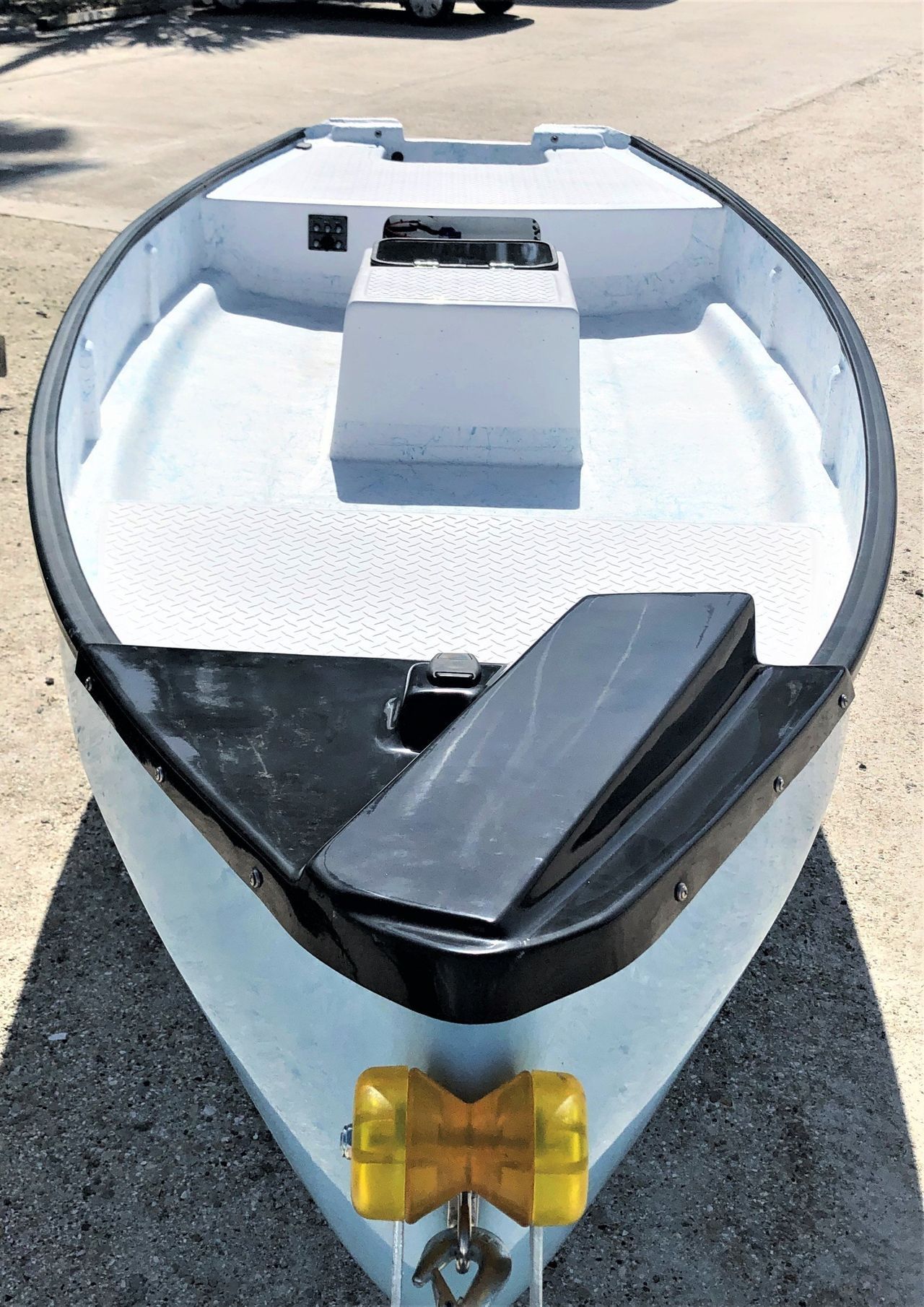 A front-facing view of a small white boat on a trailer, featuring a black bow, textured deck, and yellow bow roller.