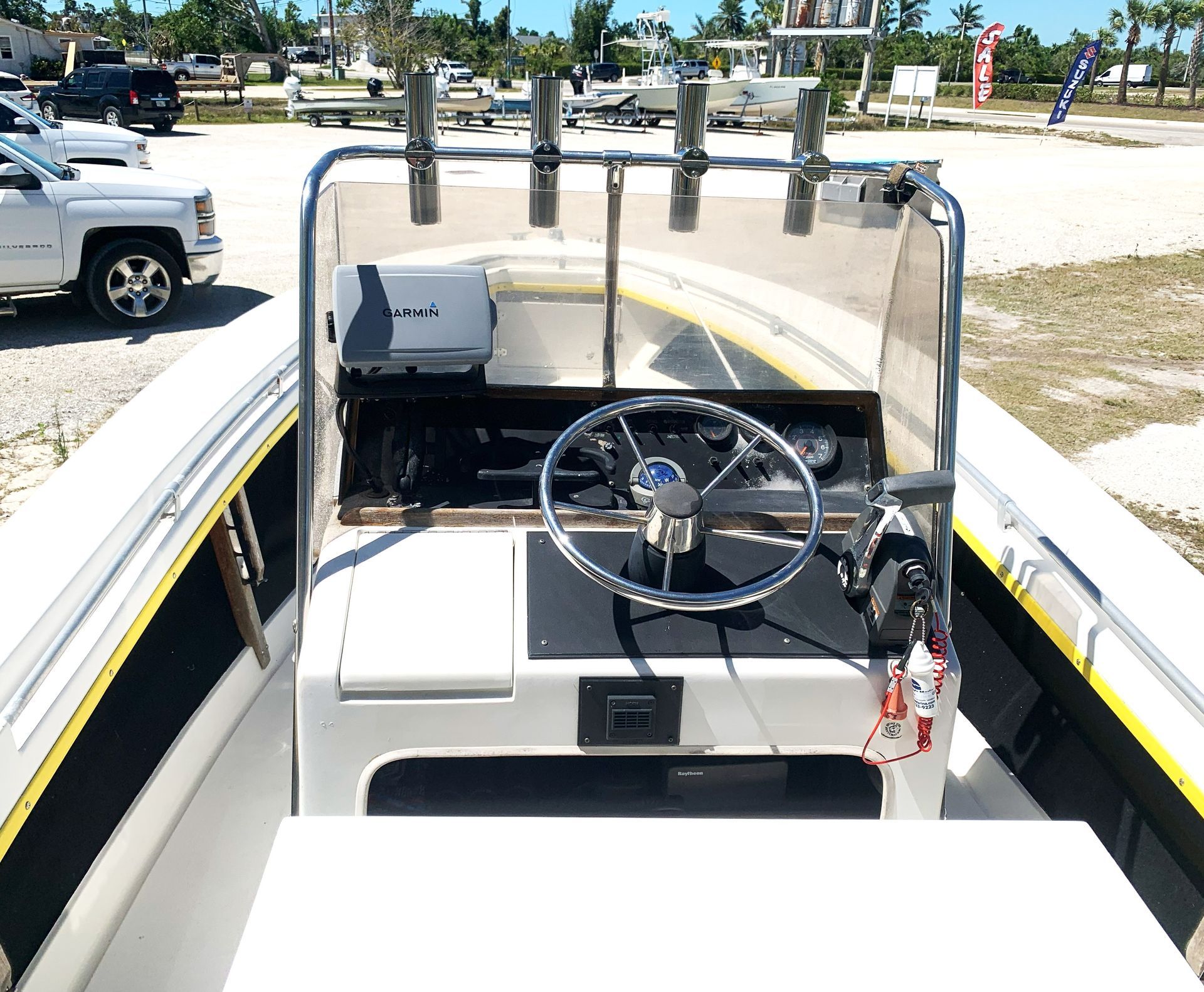 Boat cockpit with steering wheel, windshield, and fishing rod holders on a sunny day at a marina