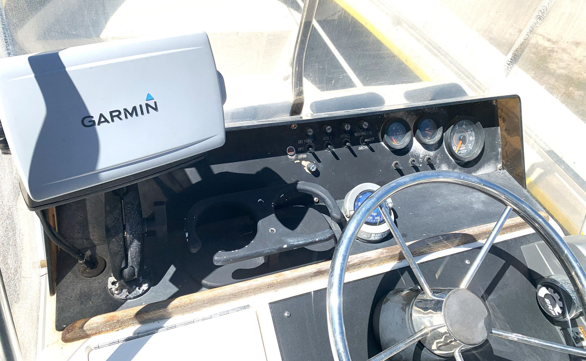 Boat dashboard with Garmin display, steering wheel, and navigation instruments in sunlight