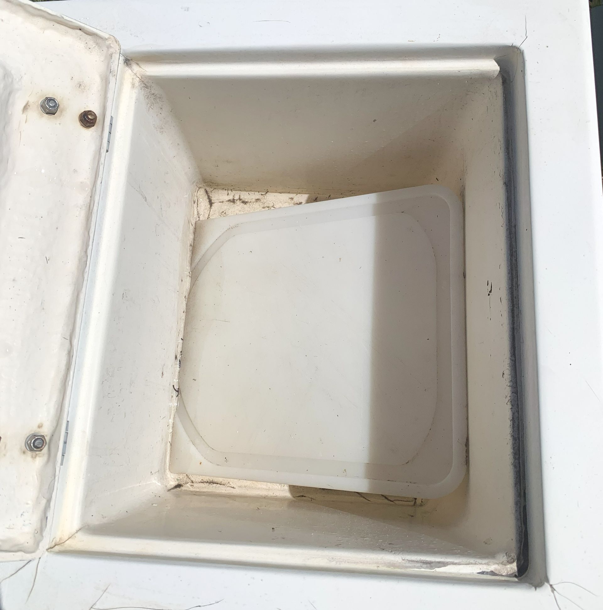 Open white cooler compartment with a small closed plastic container inside, slightly dirty corners