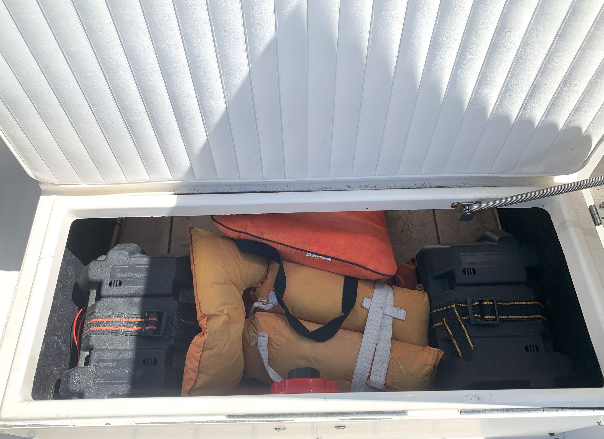 Open storage compartment with packed bags, an orange life jacket, and equipment inside.