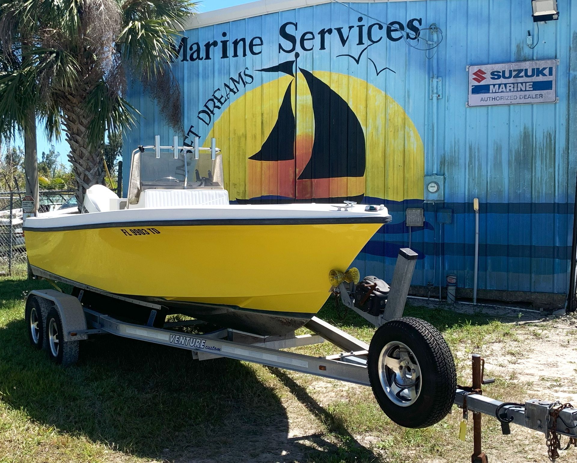 Yellow sailboat on a trailer outside a marine services building with a painted sunset mural