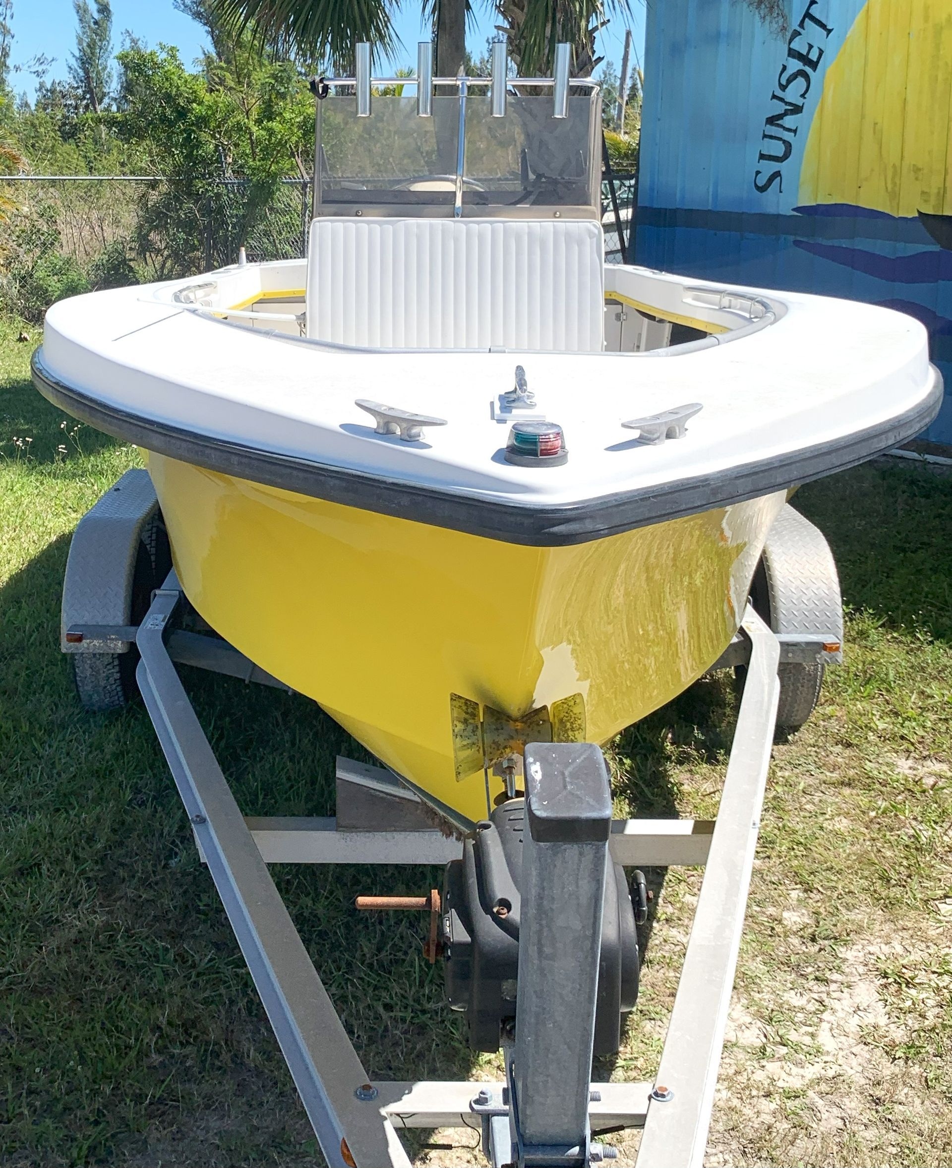 Small yellow-and-white sailboat on a trailer outdoors in a grassy yard