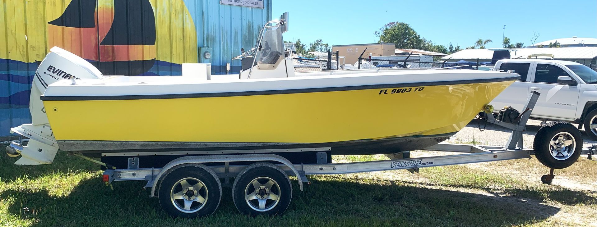 Yellow and white boat on a trailer parked on grass beside a building