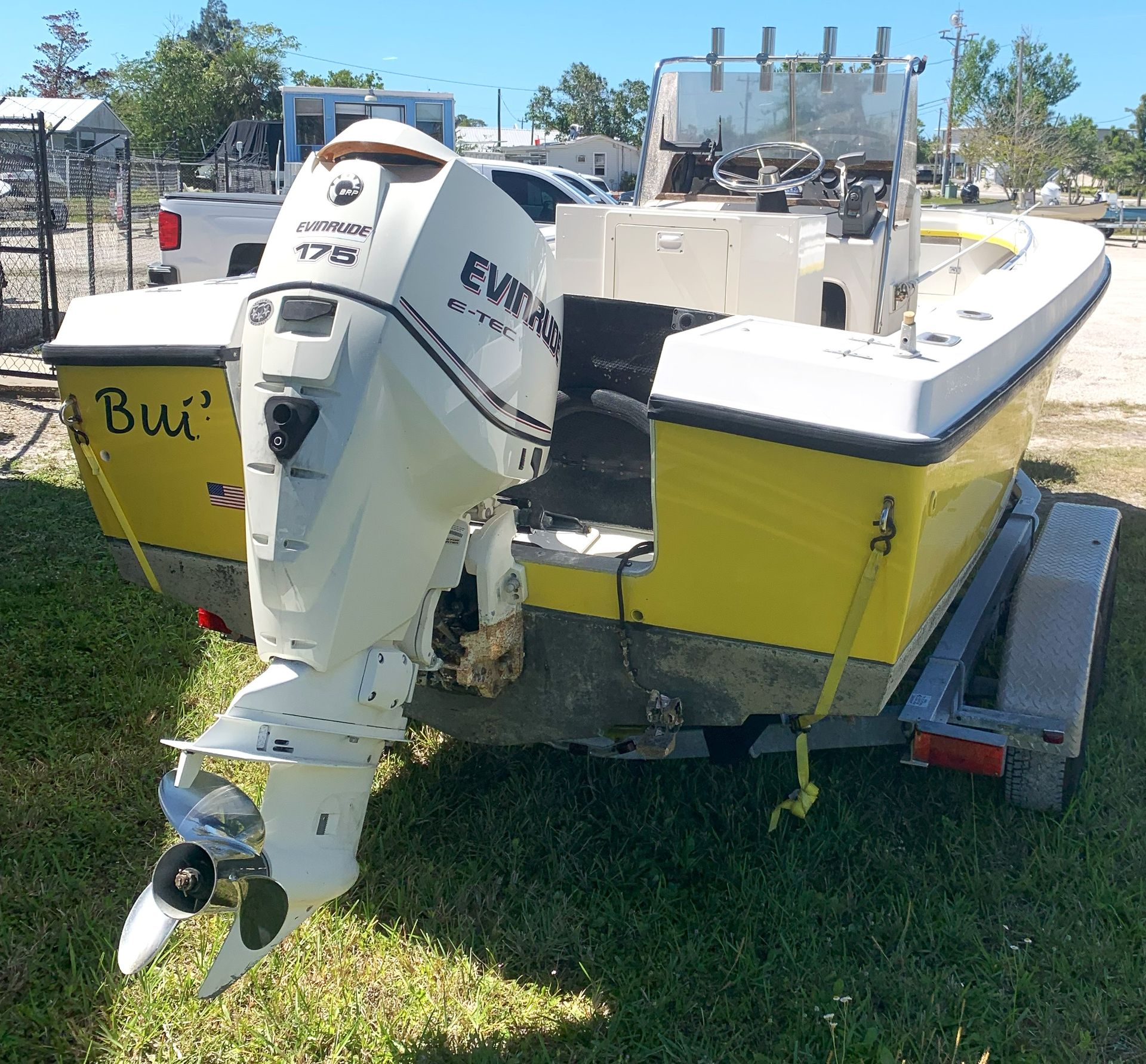 Yellow motorboat with a white outboard engine parked on a trailer in a grassy lot.