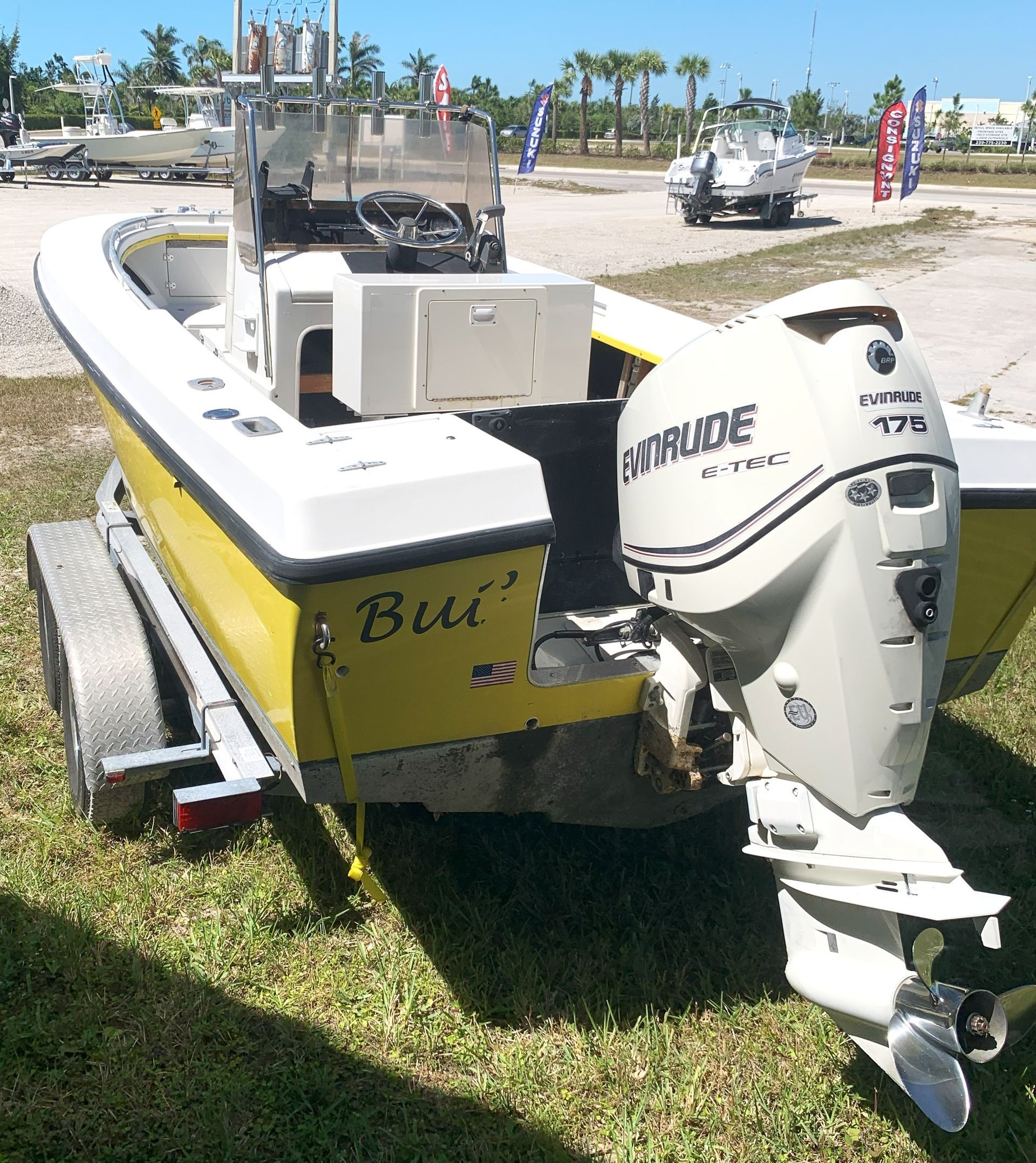 Yellow and white fishing boat with outboard motor parked on grass near water under a sunny sky
