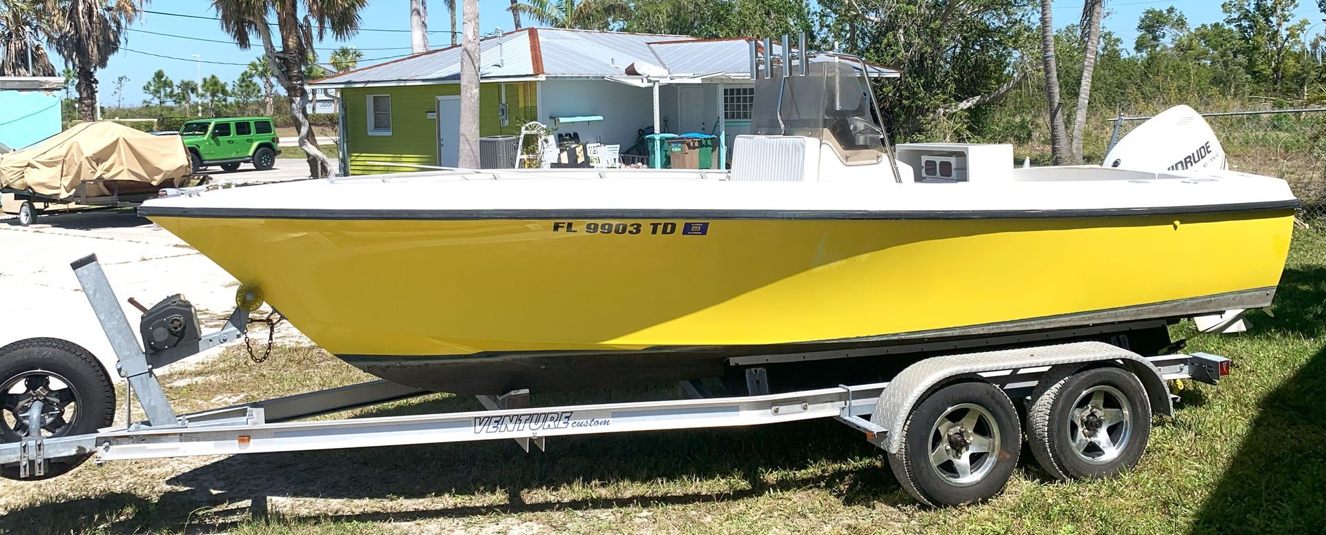 Yellow and white boat on a trailer parked on grass near a house