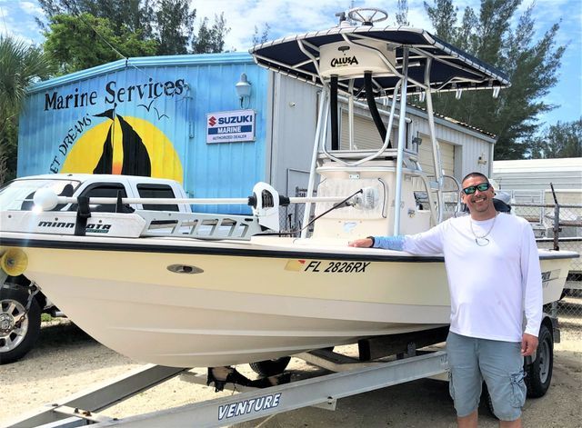 Man standing beside a cream-colored boat on a trailer in front of a marine services truck