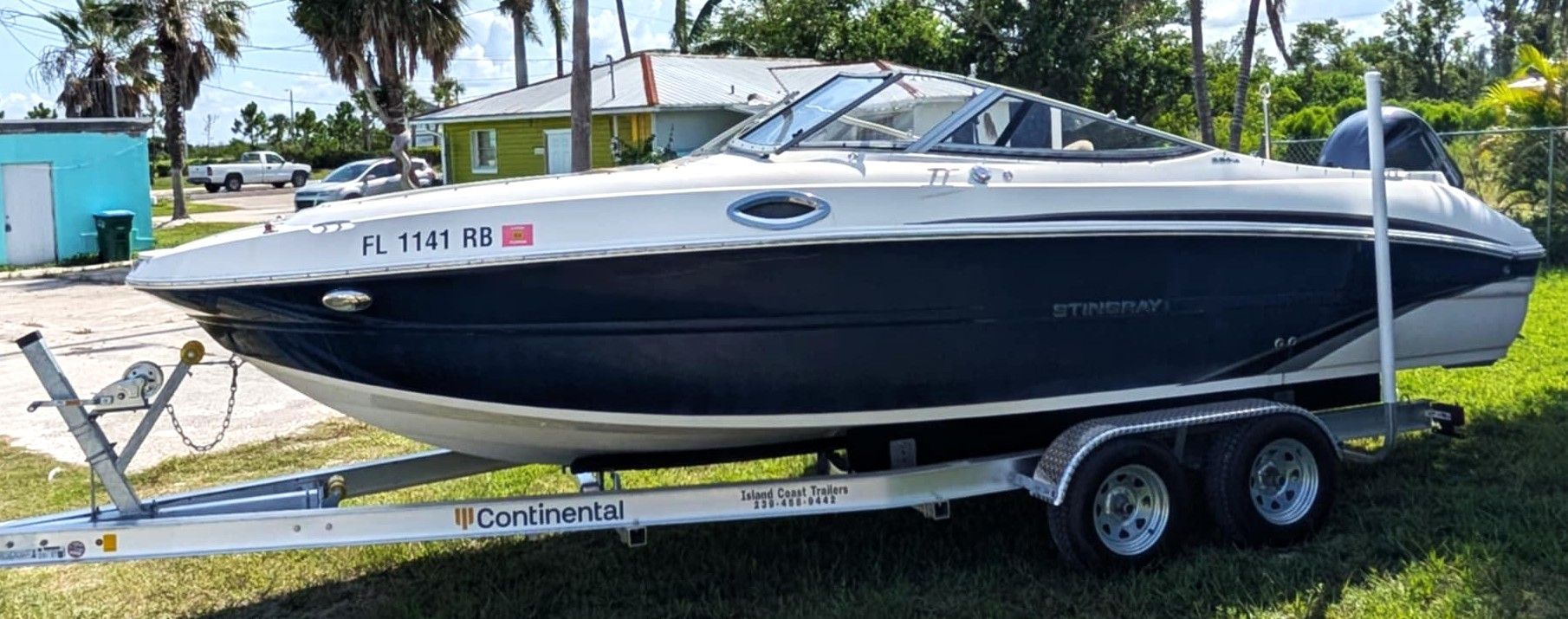 White and navy speedboat on a trailer in a grassy yard under a bright sky