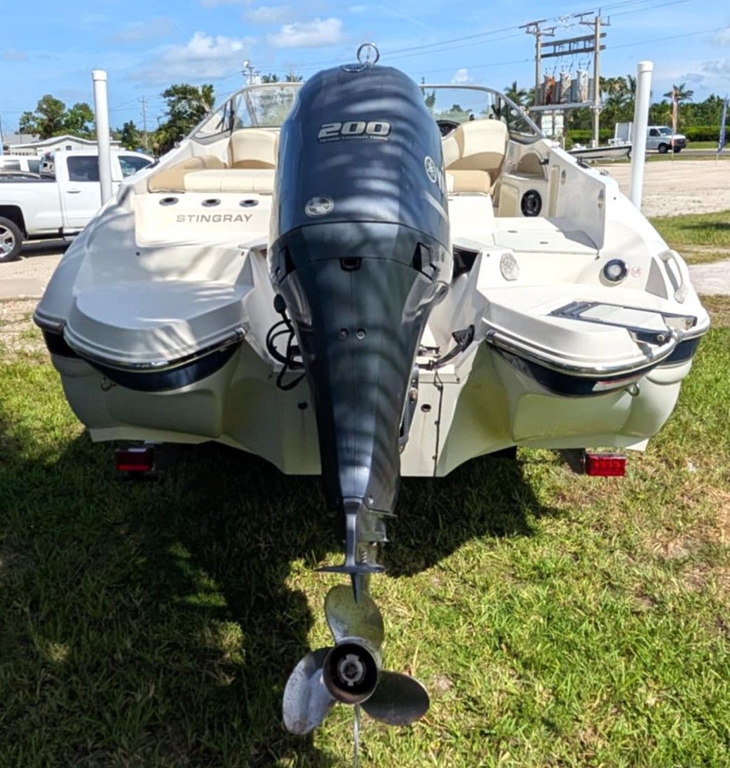 Rear view of a white boat with a black 200 HP outboard motor on grass near a road