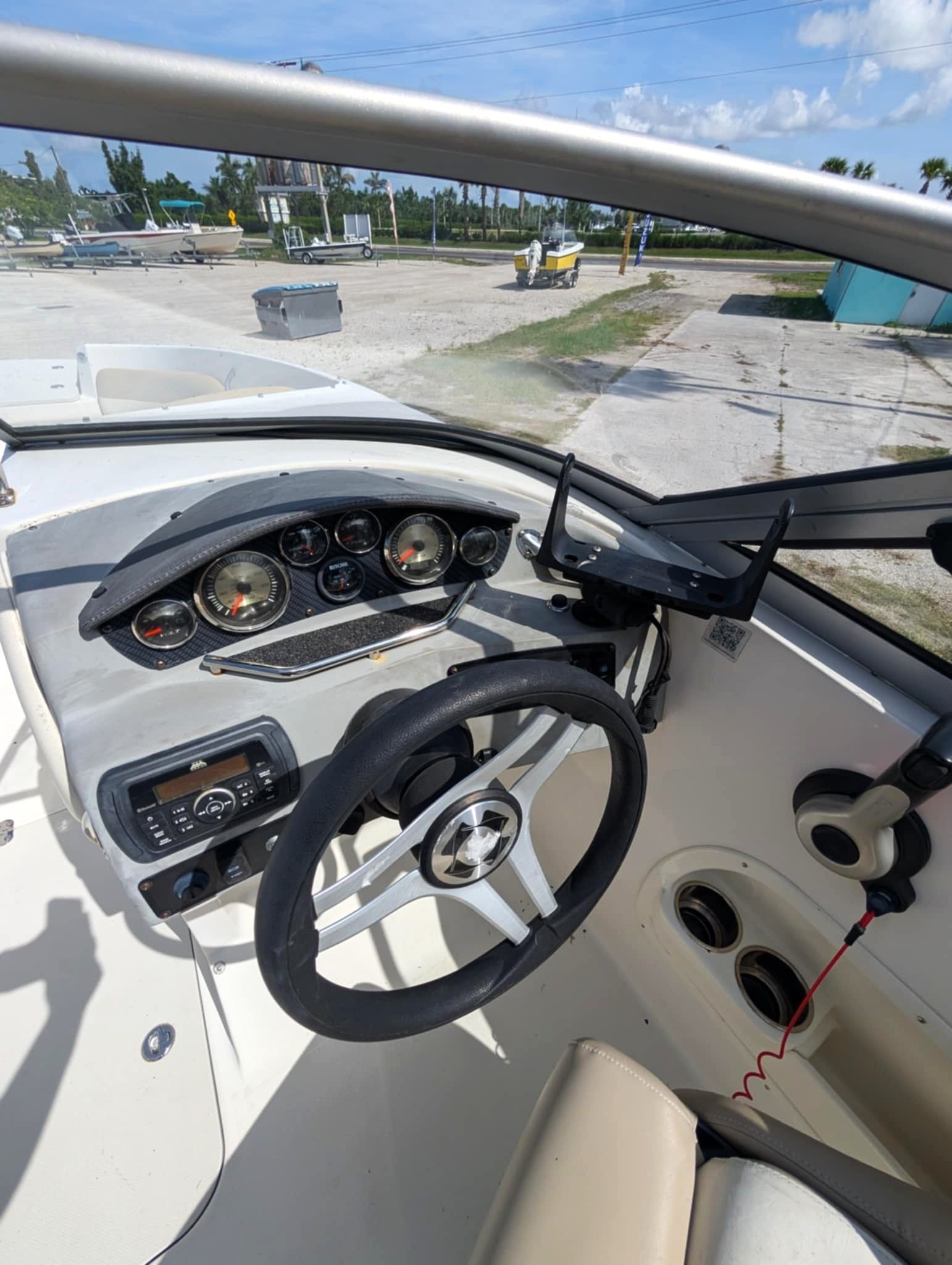 Boat helm with steering wheel, gauges, and control panel, overlooking a dock and water outside.