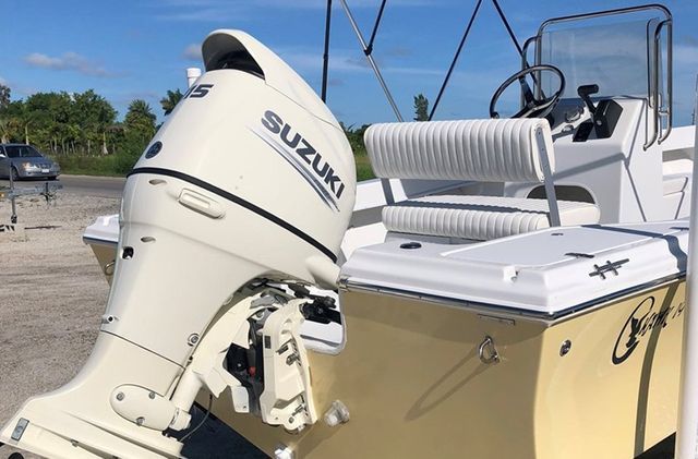 White Suzuki boat motor on a beige boat with white seats at a sunny marina