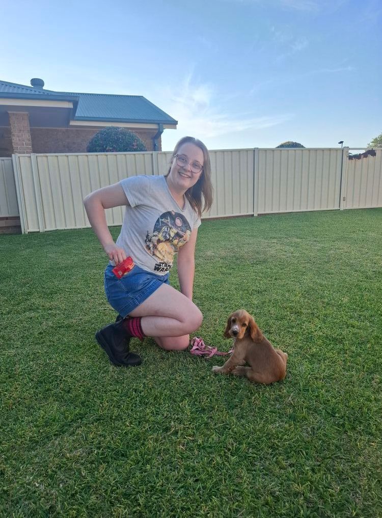 Woman crouching on grass beside a small brown dog in a backyard — Amanda's Professional K9 Training In Forster, NSW