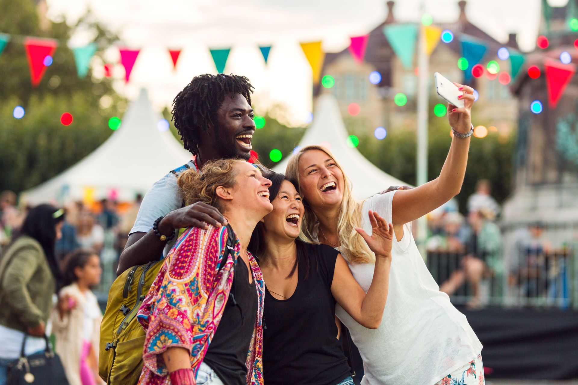Three friends smiling and taking a selfie at an outdoor festival with colorful bunting.