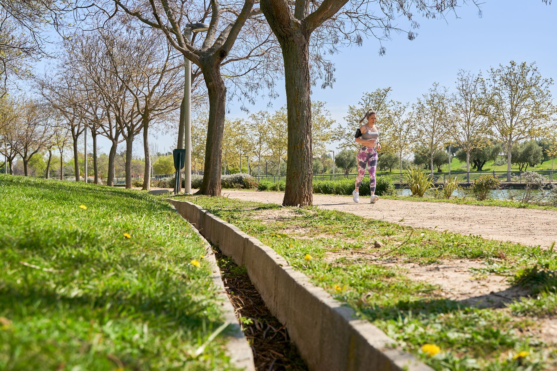 Child running on a sunny park path beside trees and green grass