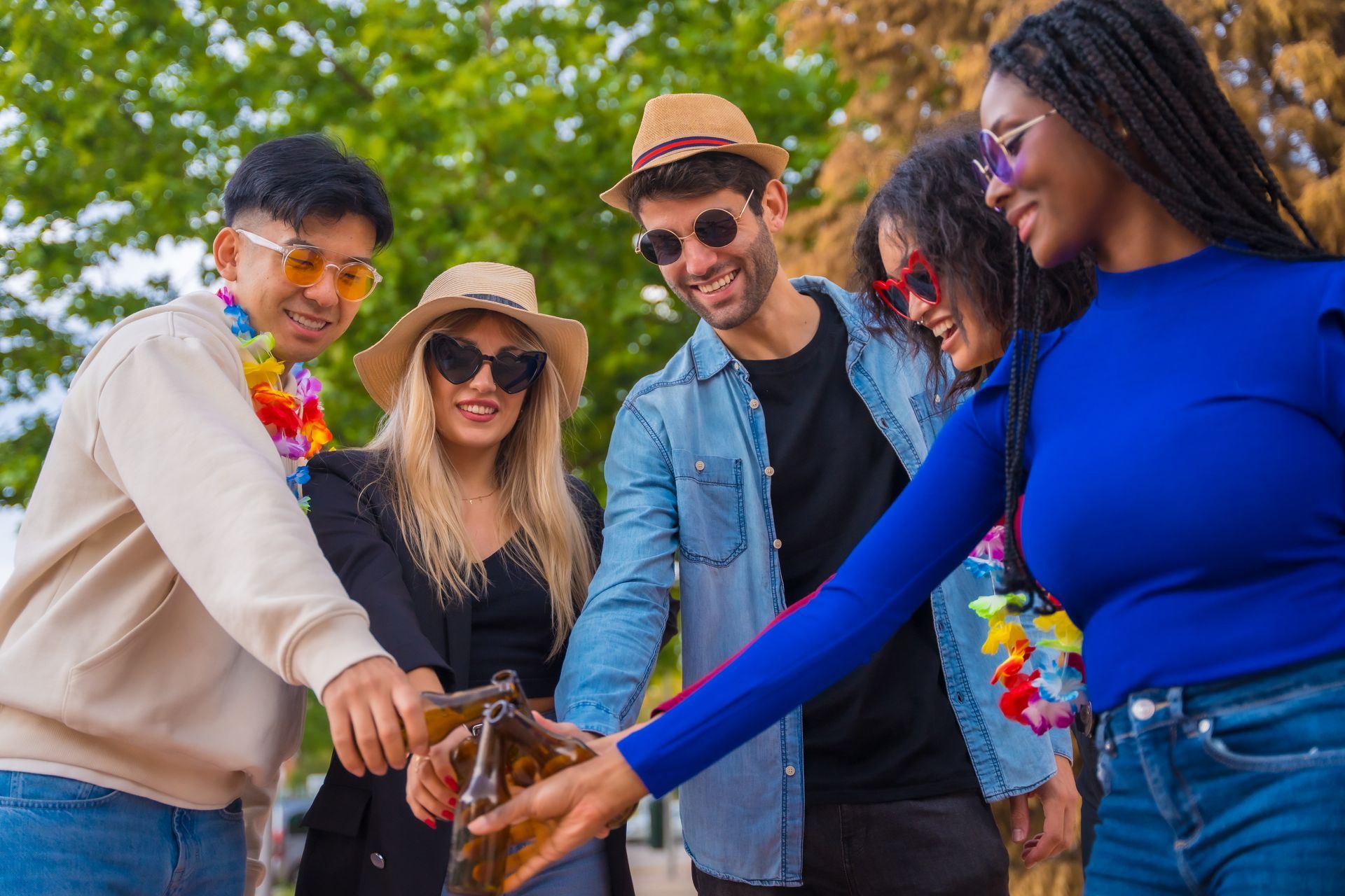Friends stacking hands together outdoors in a sunny park, smiling and wearing colorful clothes