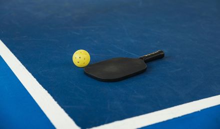Yellow pickleball and black paddle on a blue court near a white line