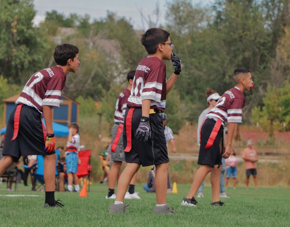 Youth soccer players in maroon jerseys line up on a grassy field during a game.