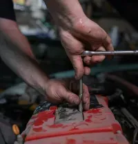 A person uses a socket wrench to tighten a bolt on a red engine cover in a dimly lit garage.