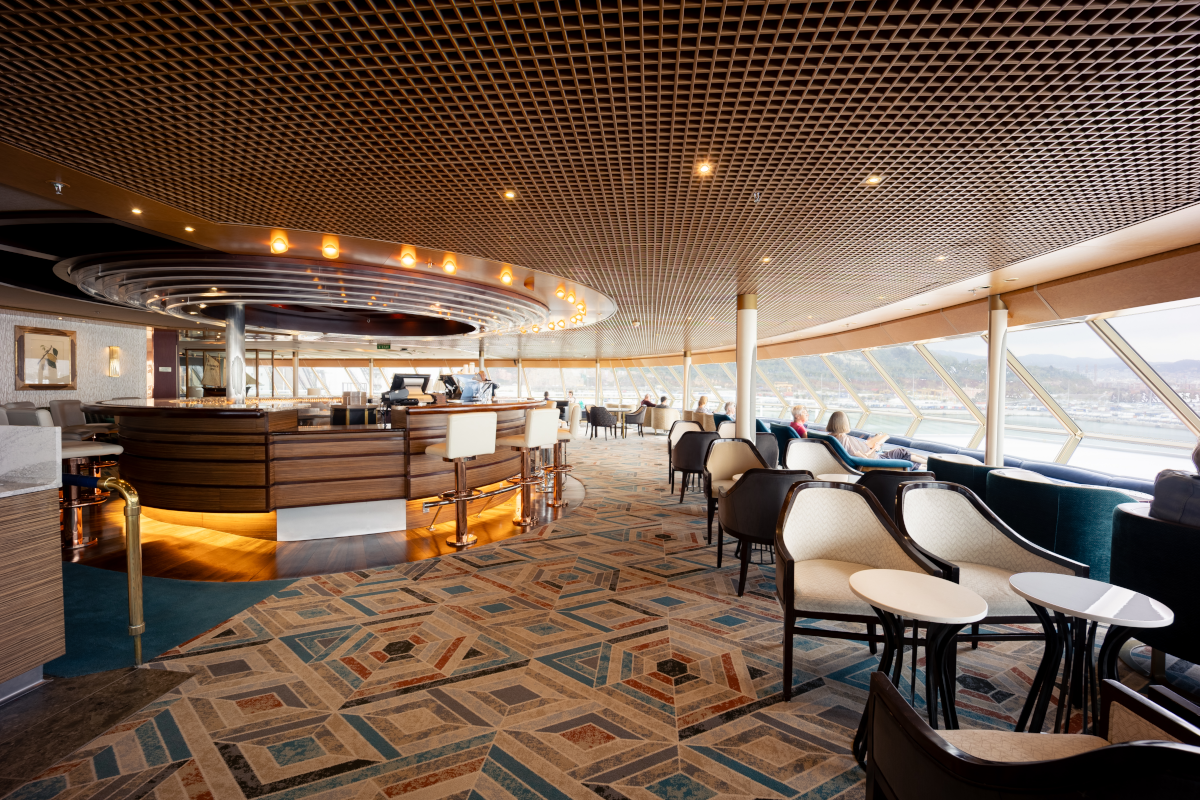 Luxurious lounge area with patterned carpet, bar, seating, and large windows.