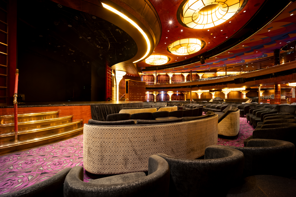 Interior of a theater. Empty stage, rows of seats, and tiered seating with gold accents.