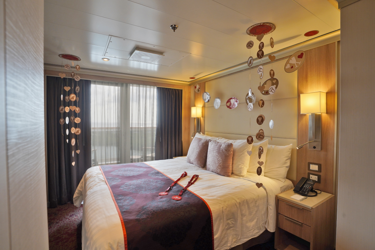 A cruise ship stateroom with a bed, nightstand, window, and decorative wall art in neutral tones.