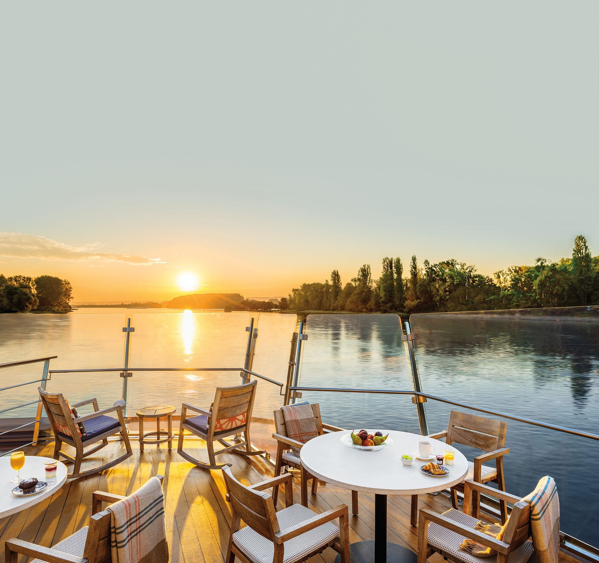 Outdoor deck with chairs and table, overlooking a river at sunset.